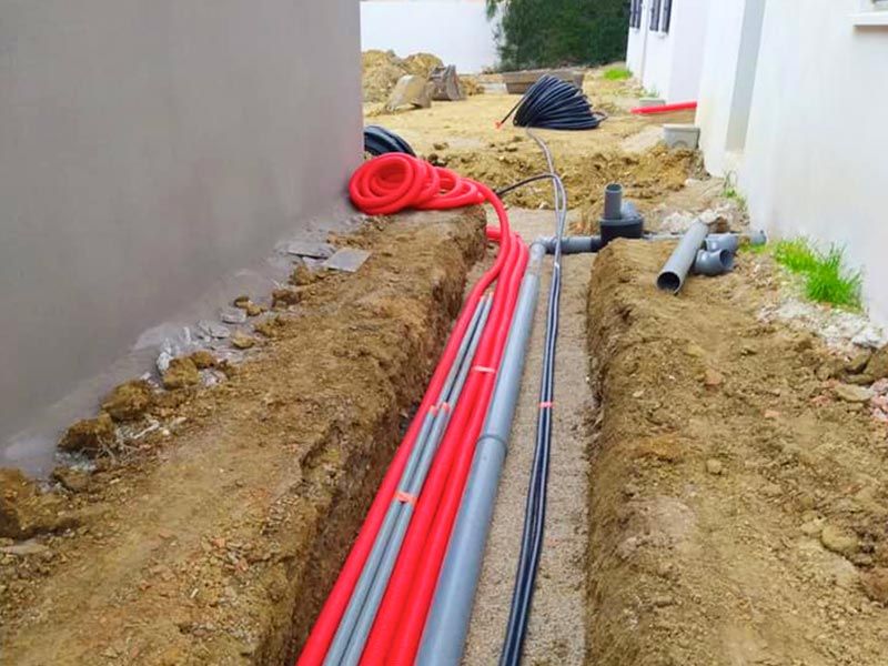 Tranchée VRD avec gaines rouges électriques et canalisations le long d'un mur — Vaucluse